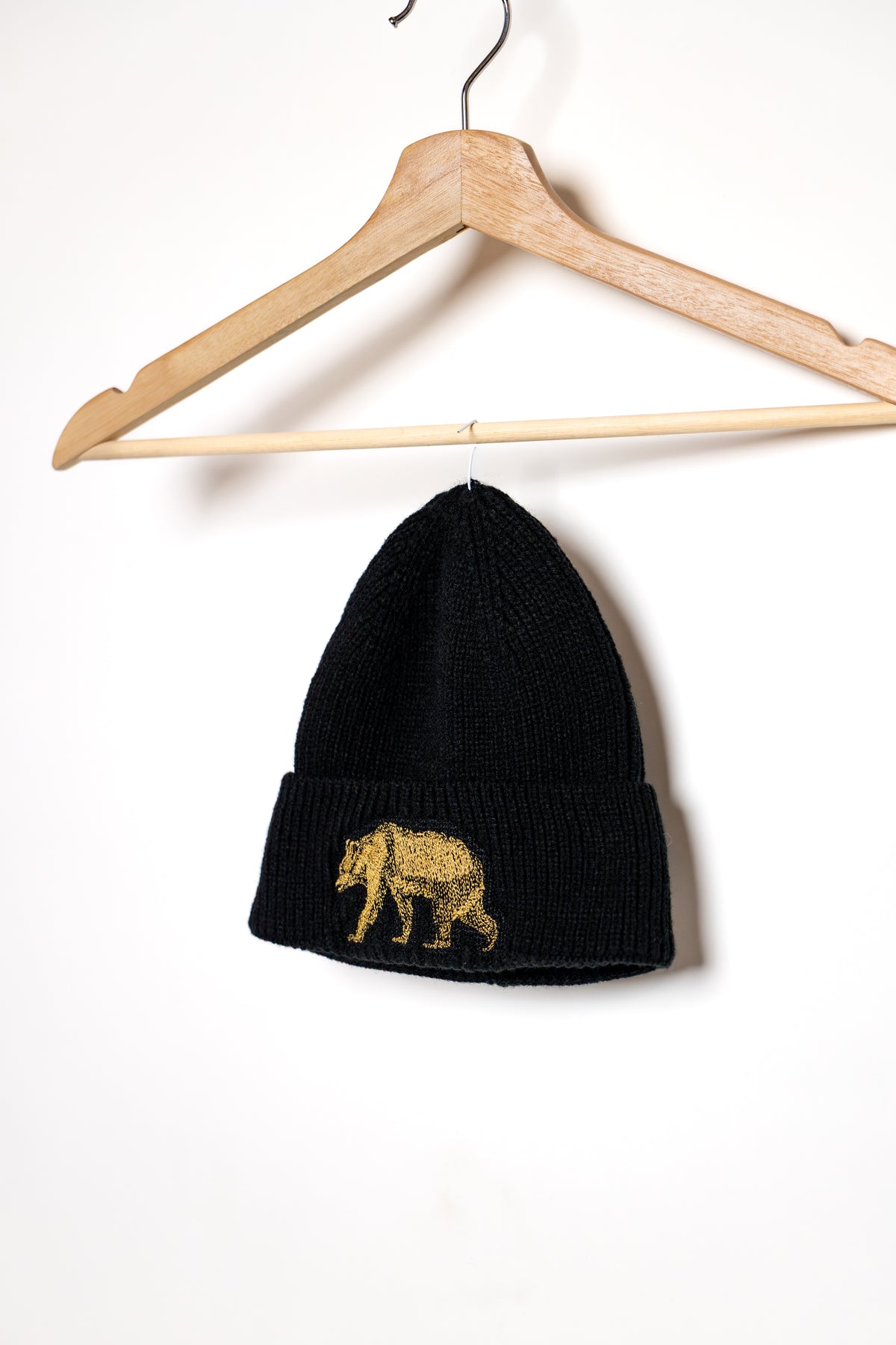 Black Pub Saint Pierre toque on a wooden hanger, gold bear on the cuff