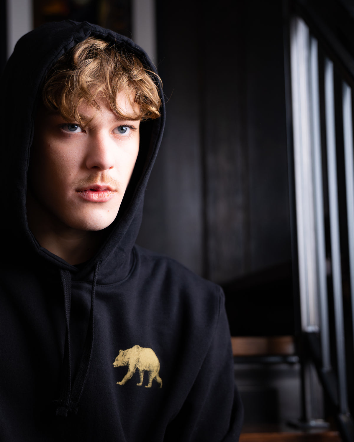 Wearing the black Pub Saint Pierre pullover hoodie with the hood up, gold bear at the chest