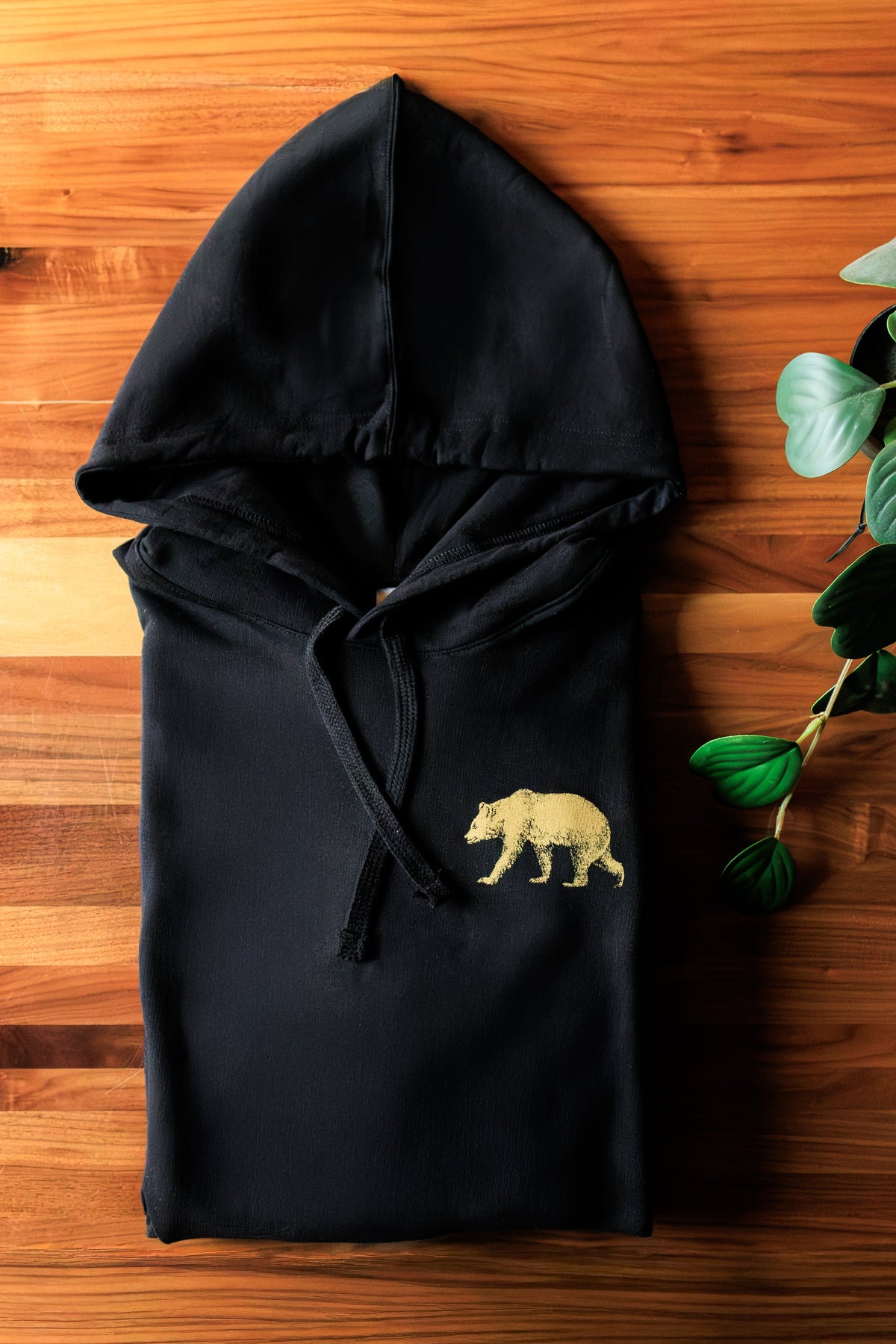 Black Pub Saint Pierre pullover hoodie folded on a walnut table with the gold bear at the chest