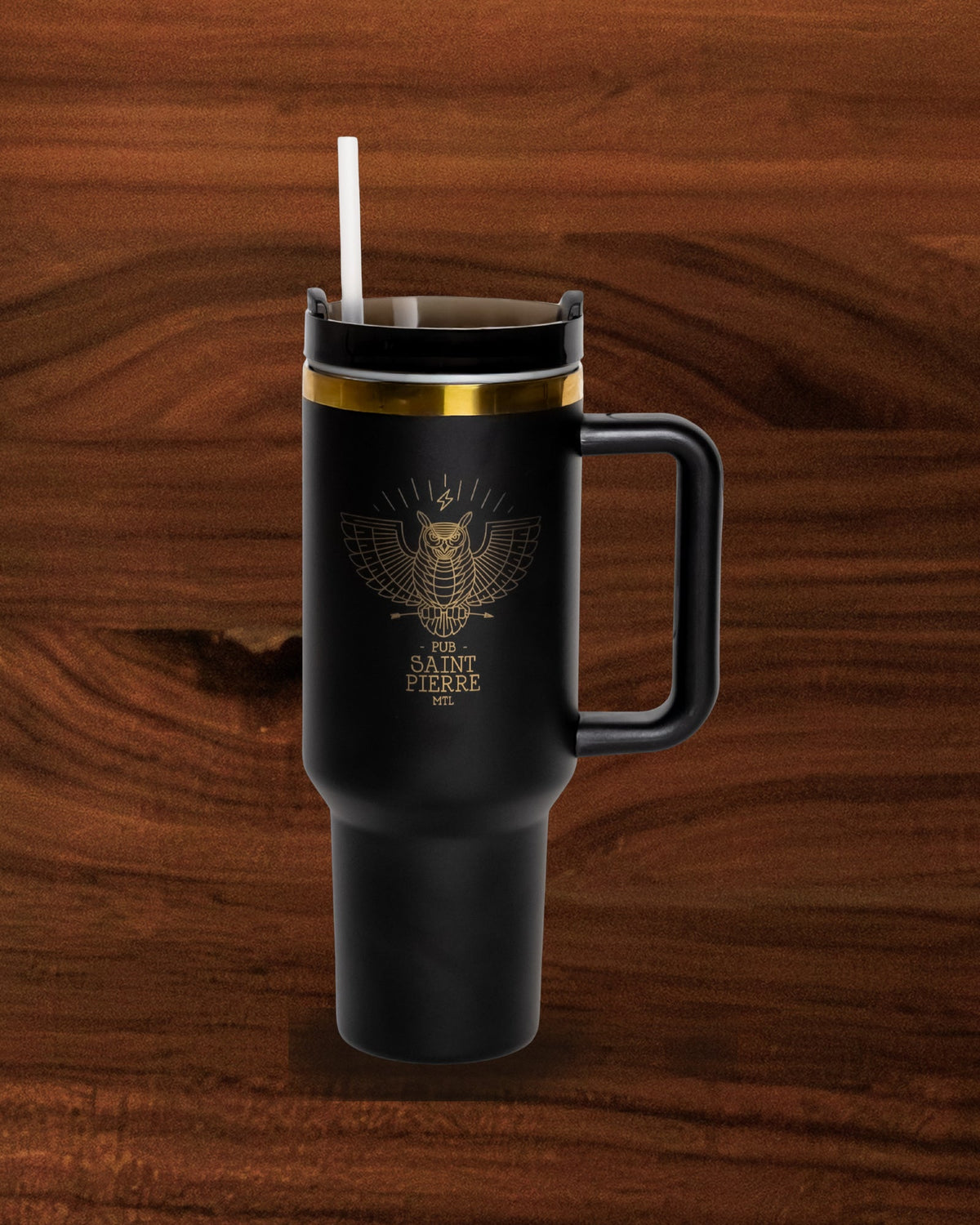 Black Pub Saint Pierre travel tumbler standing on a walnut board, gold band and gold owl crest